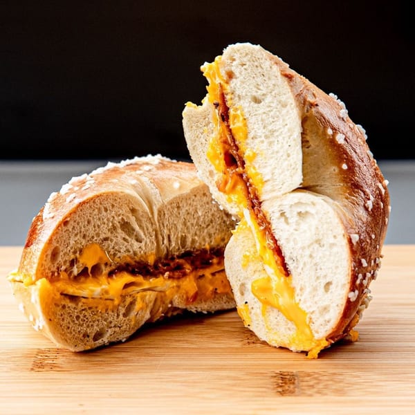 Two halves of a Big City Bagels pretzel bagel with melted cheese and bacon on a wooden board.