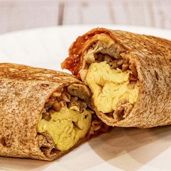 A breakfast burrito from Big City Bagels, cut in half, revealing scrambled eggs and meat.