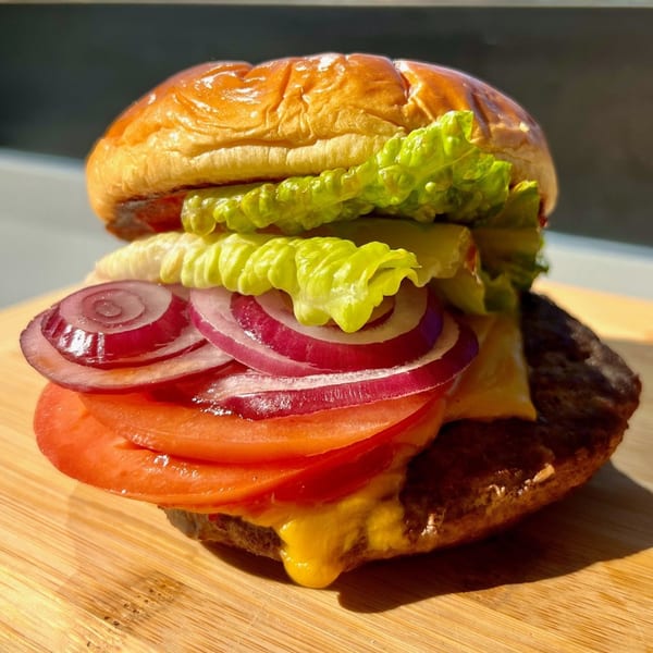 A Nathan's Famous Hot Dog burger with melted cheese, lettuce, red onion, and tomato on a bun.