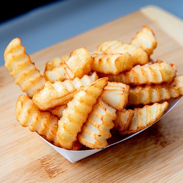 Crispy golden crinkle-cut fries in a white paper tray on a wooden surface.